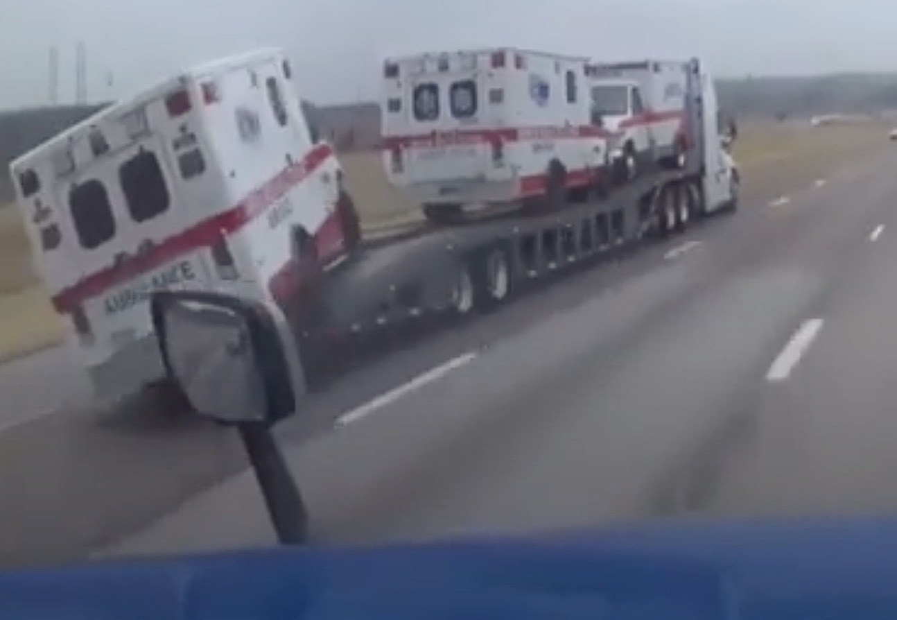 Watch an ambulance fall off a trailer and roll down the highway without a driver